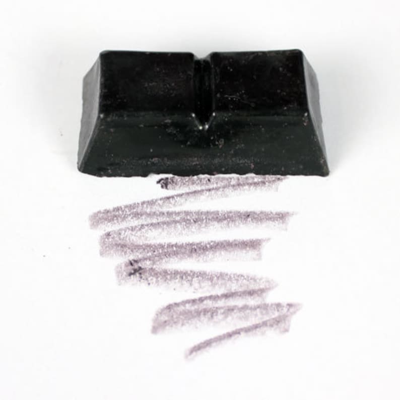 May include: A black rectangular block of charcoal for drawing, with a line of charcoal drawn on a white surface.