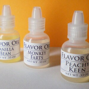 May include: Three small clear glass bottles with white labels and blue text. The labels read "Flavor Oil Vanilla Bean Net Wt .33 oz", "Flavor Oil Monkey Farts Net Wt .33 oz", and "Flavor Oil Peachy Keen Net Wt .33 oz".