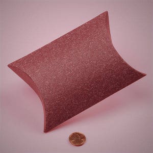 May include: A red, textured, pillow-shaped box. The box is made of a sturdy material and has a smooth, even surface. The box is perfect for packaging small gifts or items.