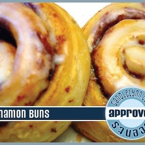 May include: Two golden brown cinnamon buns with white icing. The buns are topped with a swirl of cinnamon and have a glossy finish. The text "Cinnamon Buns" is displayed at the bottom of the image. The text "CandleLynn.com" and "approved scents" is displayed in a blue circle.