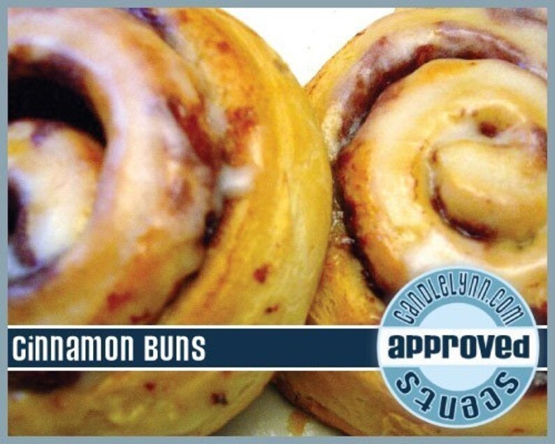 May include: Two golden brown cinnamon buns with white icing. The buns are topped with a swirl of cinnamon and have a glossy finish. The text "Cinnamon Buns" is displayed at the bottom of the image. The text "CandleLynn.com" and "approved scents" is displayed in a blue circle.