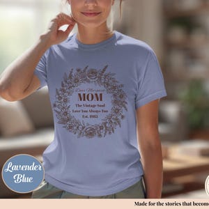 Pu&ograve; includere: T-shirt blu lavanda con un design a ghirlanda floreale e la scritta "Dear Margaret MOM The Vintage Soul Love You Always Too Est. 1983". La maglietta ha anche un logo "Handmade with Love".