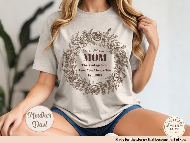Pu&ograve; includere: Una maglietta color polvere di erica con un design a ghirlanda floreale e le parole "Dear Margaret MOM" e altro testo. La maglietta include anche il testo "The Vintage Soul Love You Always Too Est. 1985".
