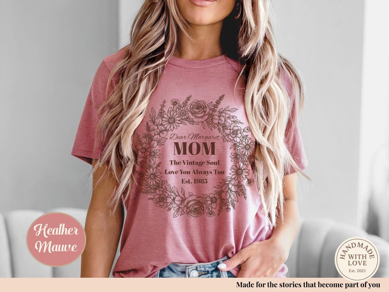 Pu&ograve; includere: T-shirt color malva heather con un design a ghirlanda floreale. Il testo recita "Dear Margaret MOM The Vintage Soul Love You Always Too Est. 1983". La maglietta &egrave; in stile casual.