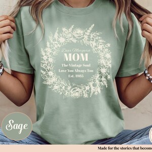 Pu&ograve; includere: T-shirt verde salvia con un design a ghirlanda floreale. Il testo sulla maglietta recita: "Dear Margaret MOM The Vintage Soul Love You Always Too Est. 1985". La maglietta &egrave; realizzata in un materiale morbido ed &egrave; comoda.