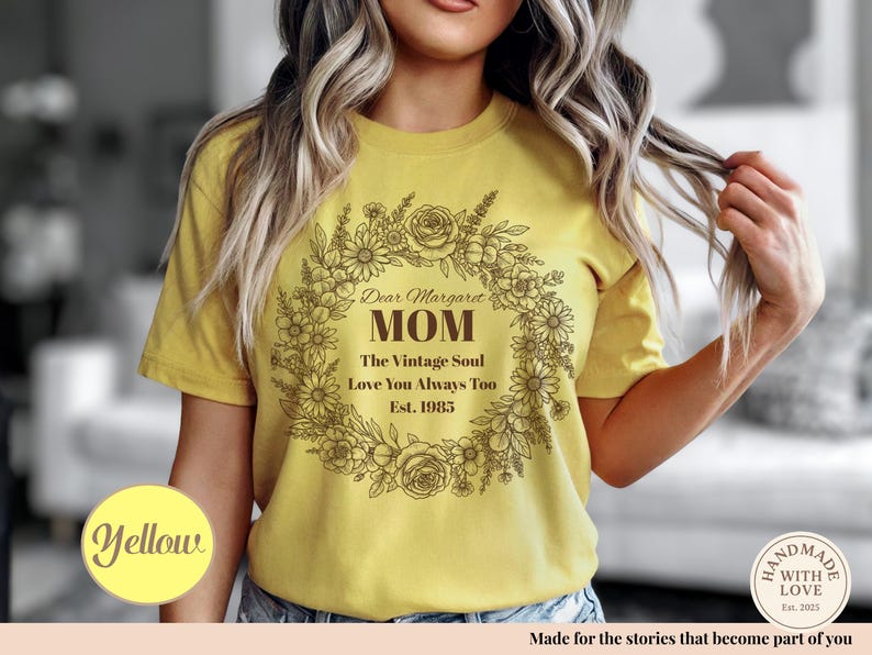 Pu&ograve; includere: T-shirt giallo senape con un design a ghirlanda floreale. Il testo all'interno della ghirlanda recita: "Dear Margaret Mom, The Vintage Soul, Love You Always Too, Est. 1985." Un cerchio giallo con la parola "Yellow" &egrave; in basso a sinistra.