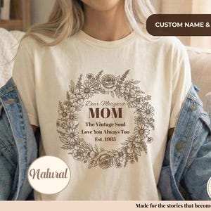 Pu&ograve; includere: T-shirt color crema con un design a ghirlanda floreale e le parole "Dear Margaret MOM The Vintage Soul Love You Always Too Est. 1985". La maglietta ha anche la parola "Natural" e "HANDMADE WITH LOVE Est. 2023" stampate.