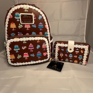 Puede incluir: Un conjunto de mochila y cartera marrones con un estampado de pastel y ribete blanco. La mochila tiene un logotipo rectangular y la cartera un cierre de botón a presión blanco. También hay una etiqueta negra con texto dorado.