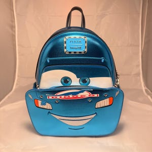 May include: Blue metallic backpack featuring Lightning McQueen from the Pixar Cars movie. The backpack has a front pocket with McQueen's face, including eyes, a smile, and the number 95. It has a top handle, adjustable straps, and a Pixar Loungefly logo.