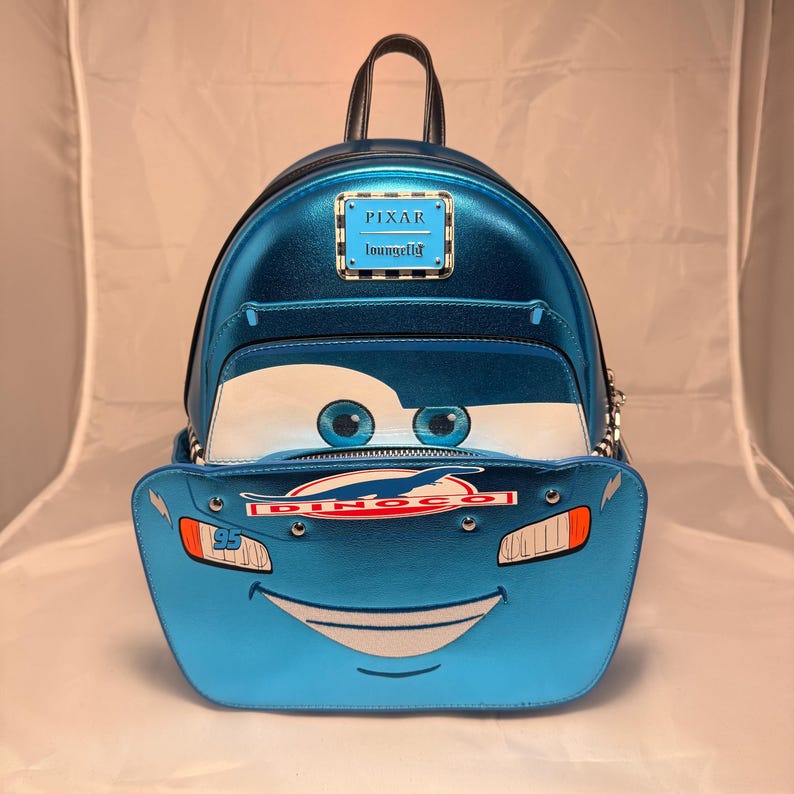 May include: Blue metallic backpack featuring Lightning McQueen from the Pixar Cars movie. The backpack has a front pocket with McQueen's face, including eyes, a smile, and the number 95. It has a top handle, adjustable straps, and a Pixar Loungefly logo.