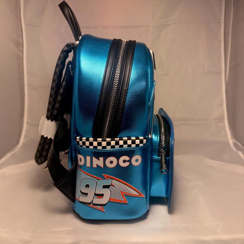 May include: A blue backpack with a shiny finish, featuring black zippers and a checkered pattern. The backpack has the word "DINOCO" and the number "95" printed on it, with a racing theme.