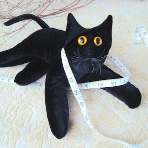 May include: A black plush cat toy with large yellow eyes. The cat is wrapped in a white measuring tape.