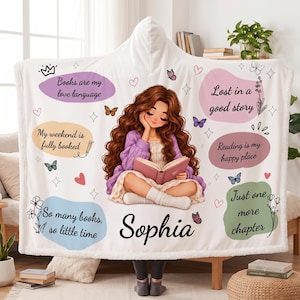 May include: A white hooded blanket featuring a central illustration of a person with long brown hair reading a book. The blanket includes colorful speech bubbles with text: Books are my love language, My weekend is fully booked, Lost in a good story, Reading is my happy place, So many books, so little time, Just one more chapter, and the name Sophia.