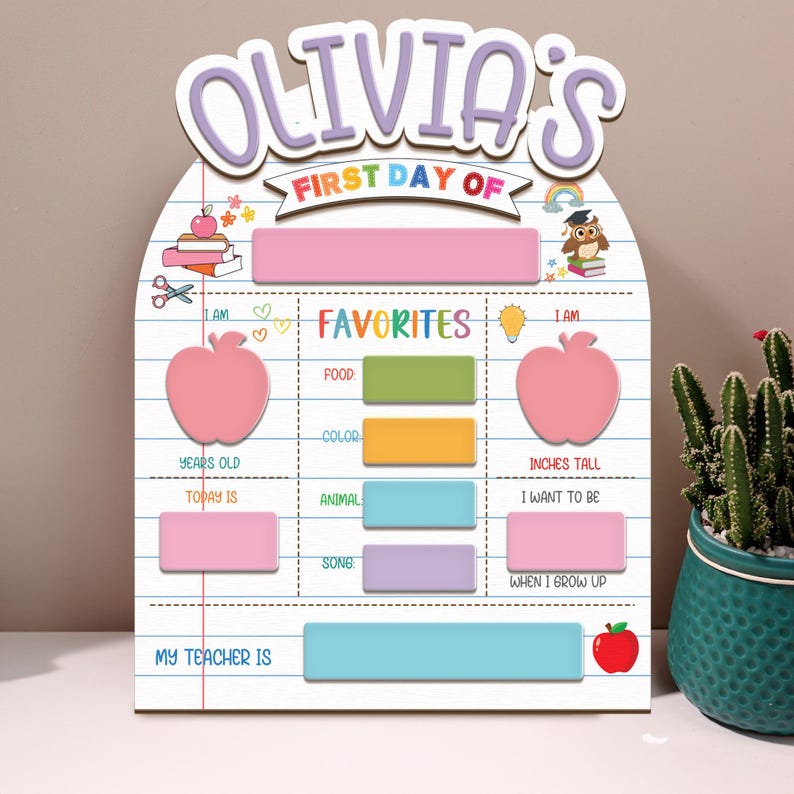 May include: A personalized wooden sign for the first day of school, featuring the name "Olivia's" in purple script. The sign includes sections for "Favorites" and other details, with a pink apple graphic and a red apple at the bottom.