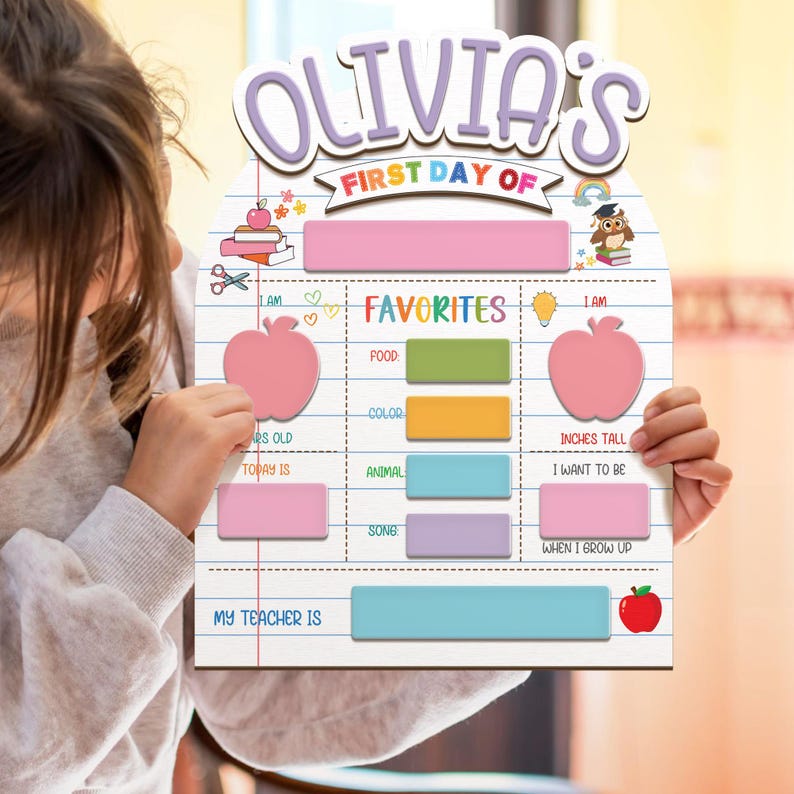 May include: A personalized wooden sign for the first day of school, featuring the name "Olivia's" in purple letters. The sign includes spaces to fill in favorites, age, and teacher's name, with apple and rainbow illustrations.