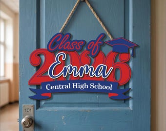 May include: A wooden graduation sign with the text "Class of 2026 Emma Central High School" in red and blue. The sign is hanging on a blue door with a rope. A graduation cap is on the right side of the sign.