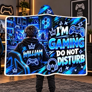 May include: A hooded blanket featuring a blue and black gaming theme with a person wearing headphones, the name WILLIAM, a game controller graphic, and the text I'M GAMING DO NOT DISTURB, finished with a white sherpa-style trim.