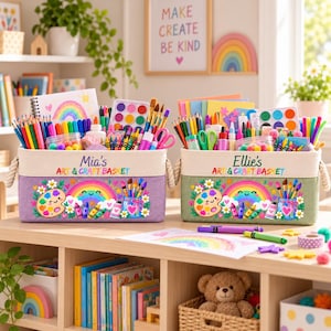 May include: Two rectangular fabric storage baskets with rope handles, one purple and one green. Each features a colorful graphic of a smiling rainbow, paint palette, and art supplies, with the text Mia's Art & Craft Basket or Ellie's Art & Craft Basket.