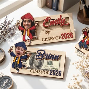 May include: Two wooden graduation frames with personalized cutouts. One frame features a photo of a woman in a graduation gown, the name "Emily", and "Class of 2026". The other frame has a photo of a man, the name "Brian", and a $100 bill.