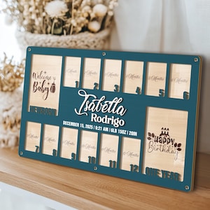 May include: A rectangular teal and light wood baby milestone photo frame featuring the name Isabella Rodrigo, birth details including December 15, 2025, 6:21 AM, 6LB 15OZ, 20IN, and twelve slots labeled 1 Month through 12 Months with Newborn and One Year sections.