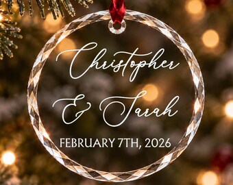 Può includere: Un ornamento circolare in vetro trasparente con bordo sfaccettato, appeso a un nastro rosso. L'ornamento è inciso con i nomi Christopher & Sarah e la data FEBRUARY 7TH, 2026 in caratteri bianchi.