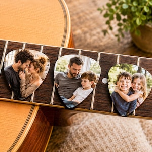 May include: Acoustic guitar fretboard with three custom guitar picks. Each pick features a family photo. The guitar is made of wood and has a natural finish. The picks are heart-shaped and have a glossy finish.