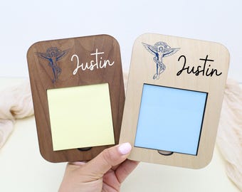 Può includere: Due portamemo in legno, uno marrone scuro e uno marrone chiaro, ciascuno con un'apertura rettangolare e un piccolo cassetto. Il nome "Justin" è scritto in corsivo. Ogni supporto ha una grafica blu di una figura alata.