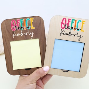 May include: Two wooden memo holders, one dark brown and one light brown, each with a rectangular opening and the text "OFFICE team Kimberly" in colorful letters. One has a yellow sticky note, the other a blue insert.