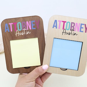May include: Two wooden memo holders with the word "ATTORNEY" in colorful letters and the name "Austin" in script. One holder is dark wood with a yellow note, the other is light wood with a blue insert.