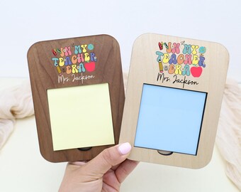 Op de afbeelding: Twee houten memohouders, één donkerbruin en één lichtbruin, elk met een rechthoekige opening en de tekst "WIN MY TEACHER ERA Mrs. Jackson" in kleurrijke letters. Eén heeft een gele plakbriefje, de andere een blauwe.