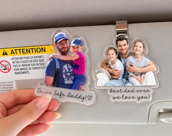 Può includere: Due clip in acrilico trasparente per aletta parasole con stampe fotografiche personalizzate. La clip sinistra mostra un uomo e un bambino con il testo "Drive Safe Daddy!" e un cuore. La destra mostra un uomo e due bambini con "best dad ever we love you!"