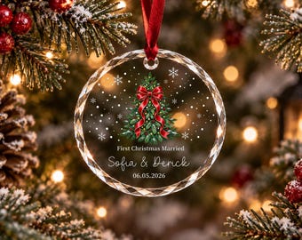 Può includere: Una decorazione natalizia in vetro circolare e sfaccettato appesa a un nastro rosso. Il centro presenta un albero di Natale verde con un fiocco rosso, fiocchi di neve bianchi e il testo: First Christmas Married, Sofia & Derick, 06.05.2026.