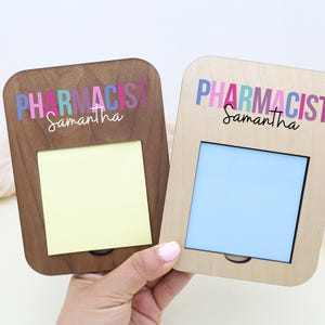 May include: Two wooden memo holders, one dark brown and one light wood, each with a rectangular opening and the word "PHARMACIST" in colorful letters above the name "Samantha". One has a yellow sticky note, the other a blue insert.