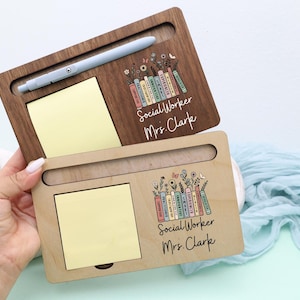 May include: Two wooden desk organizers, one dark brown and one light brown, each with a slot for a pen, a yellow sticky note pad, and a floral and book design. The text "Social Worker Mrs. Clark" is printed on each organizer.