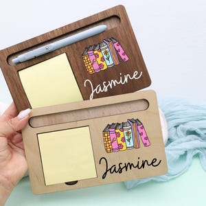 May include: Two wooden desk organizers, one dark brown and one light brown, each with a slot for a pen, a notepad, and a decorative illustration of books. The name "Jasmine" is written on each organizer.