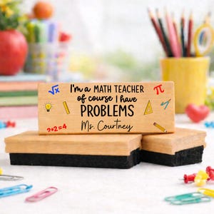 Puede incluir: Organizador de escritorio de madera con el texto "I'm a MATH TEACHER of course I have PROBLEMS Ms. Courtney" y s&iacute;mbolos matem&aacute;ticos. Tiene un acabado de madera marr&oacute;n claro y una base de fieltro negro.