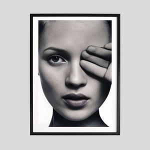 Può includere: Ritratto in bianco e nero incorniciato di una donna con la mano che copre un occhio. L'immagine è un primo piano, focalizzato sul viso e sui dettagli. La cornice è nera.