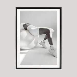 May include: Black and white framed print featuring a person in white athletic wear, resting on a white exercise ball. The image is a minimalist composition, emphasizing form and light, suitable for fitness or wellness themes.