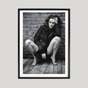 Könnte beinhalten: Schwarz-weiß gerahmtes Foto einer Person, die hockt und eine dunkle Jacke und Absätze trägt. Der Hintergrund zeigt eine Backsteinmauer und einen Holzboden. Die Person hat die Hand am Kopf.