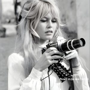 May include: Monochrome image of a person holding a vintage camera with a long lens. The camera features white rings and a black strap with white polka dots. The person is wearing a white blouse and has long blonde hair.