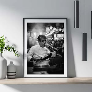 Peut inclure: Tirage encadr&eacute; en noir et blanc d'un chef en veste blanche, tenant une po&ecirc;le et une bouteille, semblant boire &agrave; la bouteille. L'arri&egrave;re-plan montre une sc&egrave;ne de restaurant anim&eacute;e avec des gens et des lumi&egrave;res.