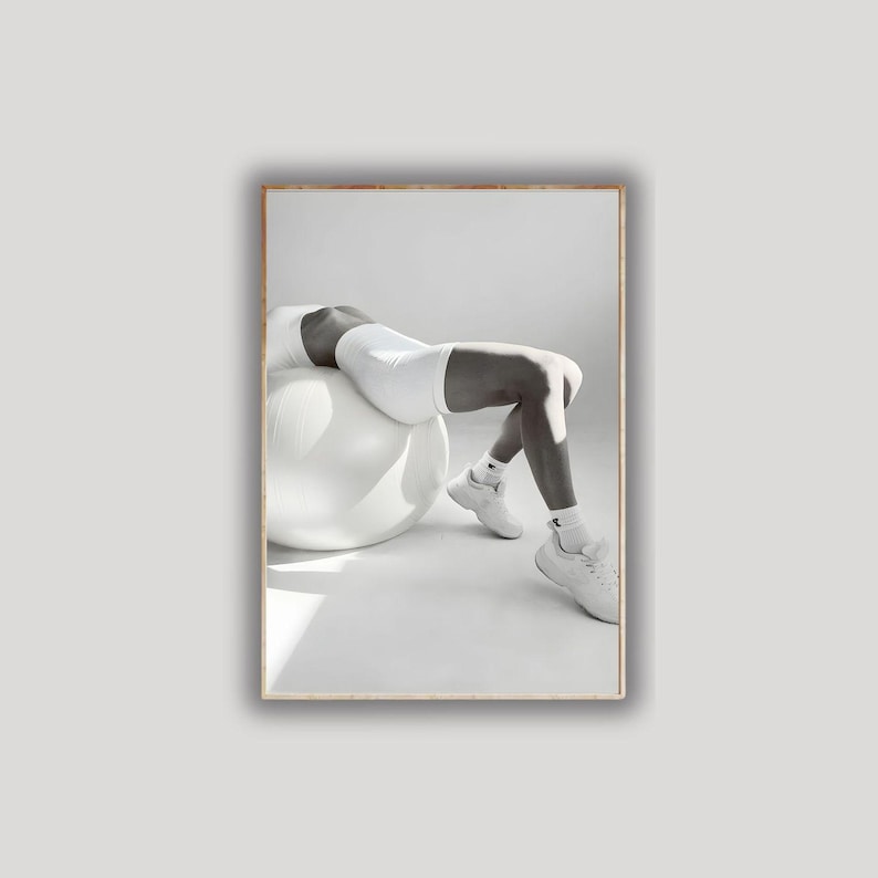 May include: Black and white photograph of a person wearing white athletic shorts, a sports bra, socks, and sneakers, resting on a large white exercise ball. The image is set against a plain white background.