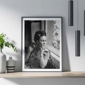 Pu&ograve; includere: Stampa incorniciata in bianco e nero di una donna che fuma una sigaretta. La donna indossa un top a quadri e ha i capelli raccolti in uno chignon con un fiore. La stampa &egrave; esposta su una mensola di legno con un vaso e illuminazione decorativa.