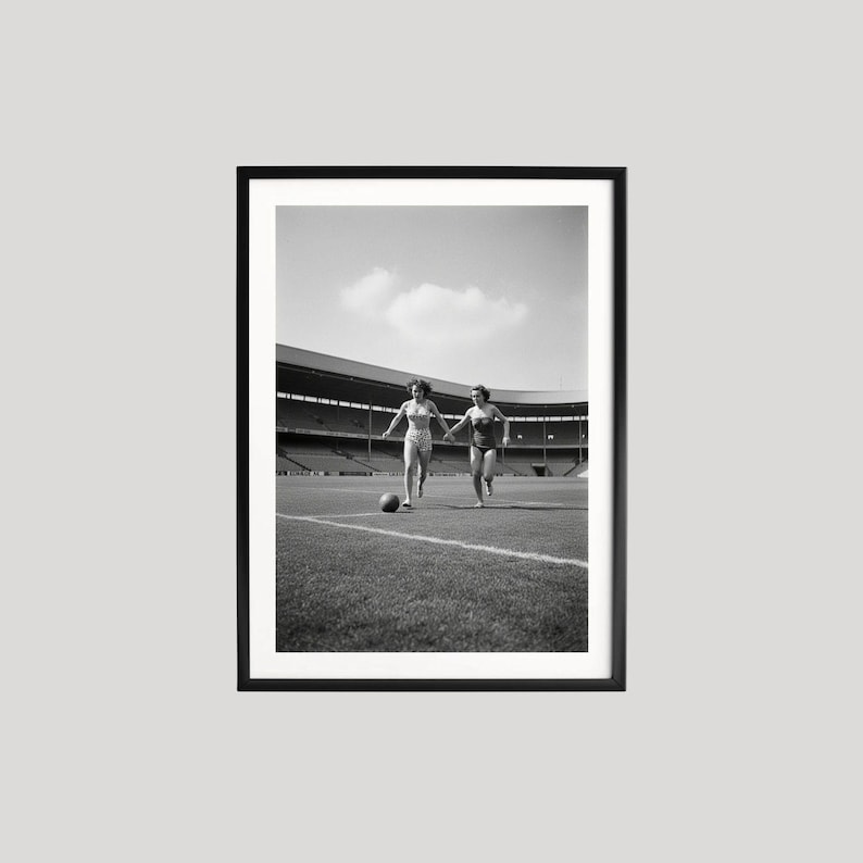 K&ouml;nnte beinhalten: Schwarz-wei&szlig; gerahmtes Foto von zwei Personen, die auf einem Fu&szlig;ballfeld laufen und einem Fu&szlig;ball hinterherjagen. Der Hintergrund zeigt ein Stadion mit Sitzreihen unter einem bew&ouml;lkten Himmel.