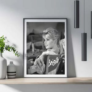 Pu&ograve; includere: Stampa incorniciata in bianco e nero con un ritratto di Brigitte Bardot. L'immagine mostra Bardot seduta, con il nome "Brigitte" visibile sullo schienale della sedia. La stampa &egrave; esposta su una mensola di legno.
