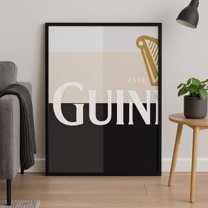 Könnte beinhalten: Schwarz-weißes Poster mit dem Wort "GUINNESS" in weißen Buchstaben und einem goldenen Harfenlogo mit dem Text "ESTD" darüber. Das Poster hat einen schwarzen Rahmen.