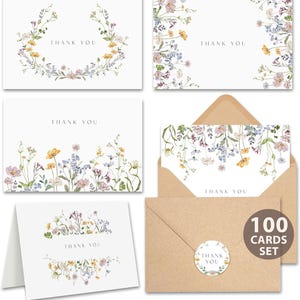 May include: A set of white thank you cards with floral watercolor designs in yellow, pink, and purple. The cards feature the text "THANK YOU" and are accompanied by kraft paper envelopes and a sticker that reads "THANK YOU". The set includes 100 cards.