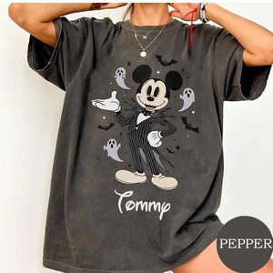 May include: A charcoal gray short-sleeve t-shirt featuring a graphic of a cartoon mouse dressed in a black pinstripe suit, surrounded by small white ghosts, black bats, and stars. The name Tommy is printed in white script below the graphic.