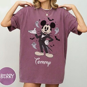 May include: A berry-colored crewneck t-shirt featuring a graphic of Mickey Mouse dressed in a pinstriped suit, surrounded by small ghosts, bats, and stars. The name Tommy is printed in white script below the character. The fabric has a vintage wash.