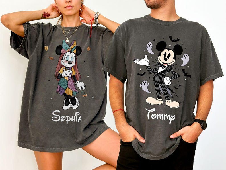 May include: Two charcoal gray t-shirts featuring Disney characters. The left shirt displays Minnie Mouse in a patchwork dress with the name Sophia. The right shirt shows Mickey Mouse in a pinstripe suit with ghosts and bats, labeled Tommy.